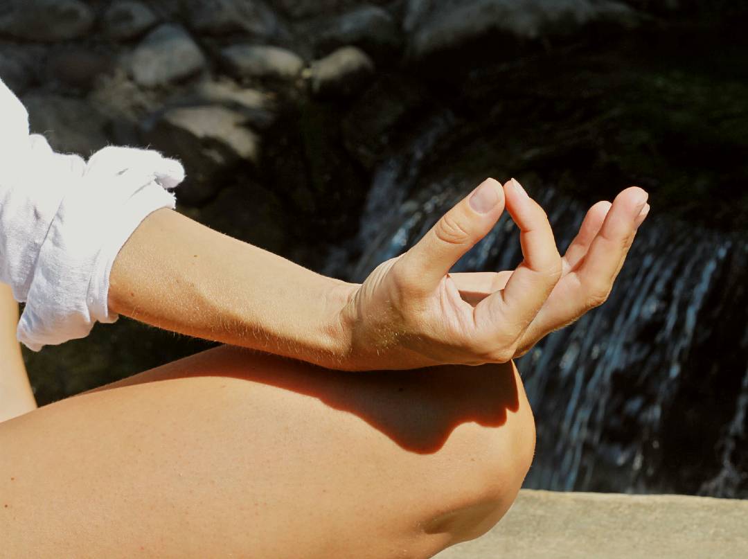 hand of person doing yoga with waterfall in background